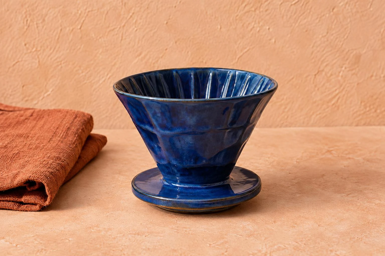 Remove shadow from photo — blue ceramic dripper and saucer on a peach surface with rust linen.